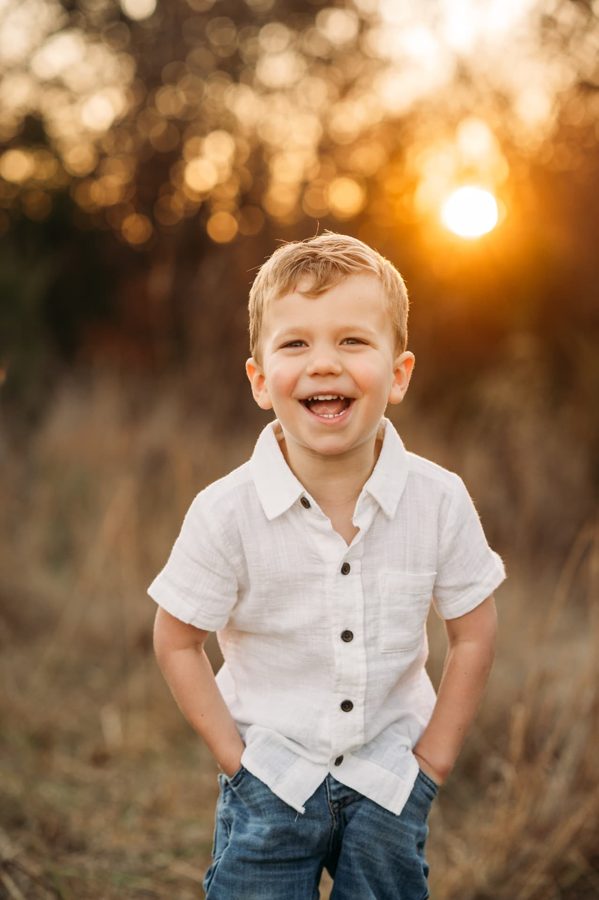 Little boy in a white shirt laughing in a golden sunset field — family photography in the Kansas City area