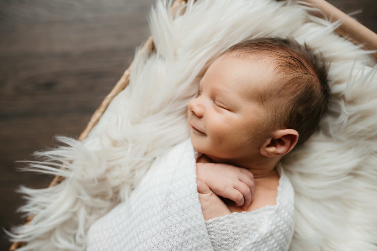 Newborn asleep in a basket on white faux fur in a sunlit room — newborn photography in the Kansas City area