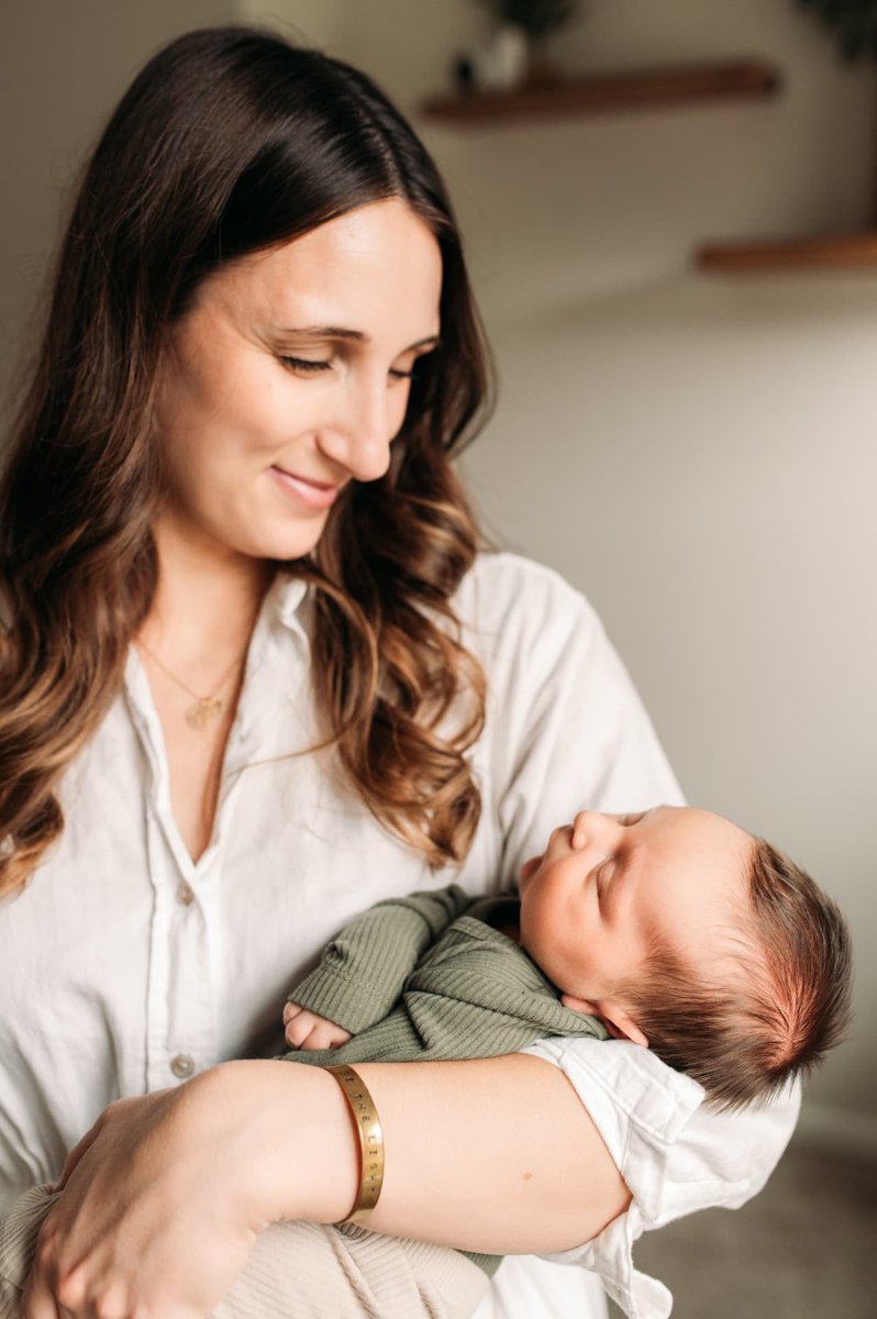 Mother smiling down at her newborn son in soft window light — newborn photography in the Kansas City area