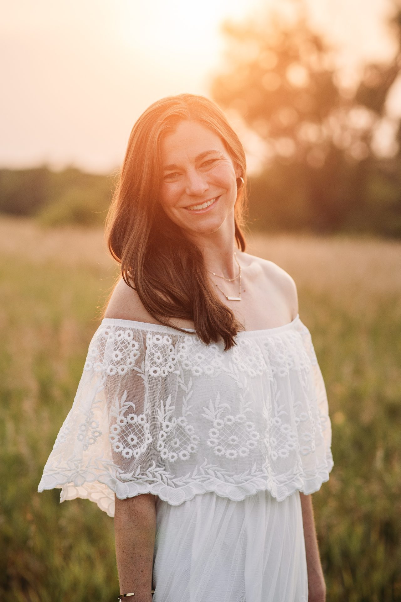 Rachel Cherry in a white lace dress, smiling in a field at golden hour