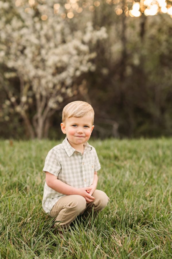 Little boy in a gingham shirt kneeling in spring grass at golden hour — family photography in the Kansas City area