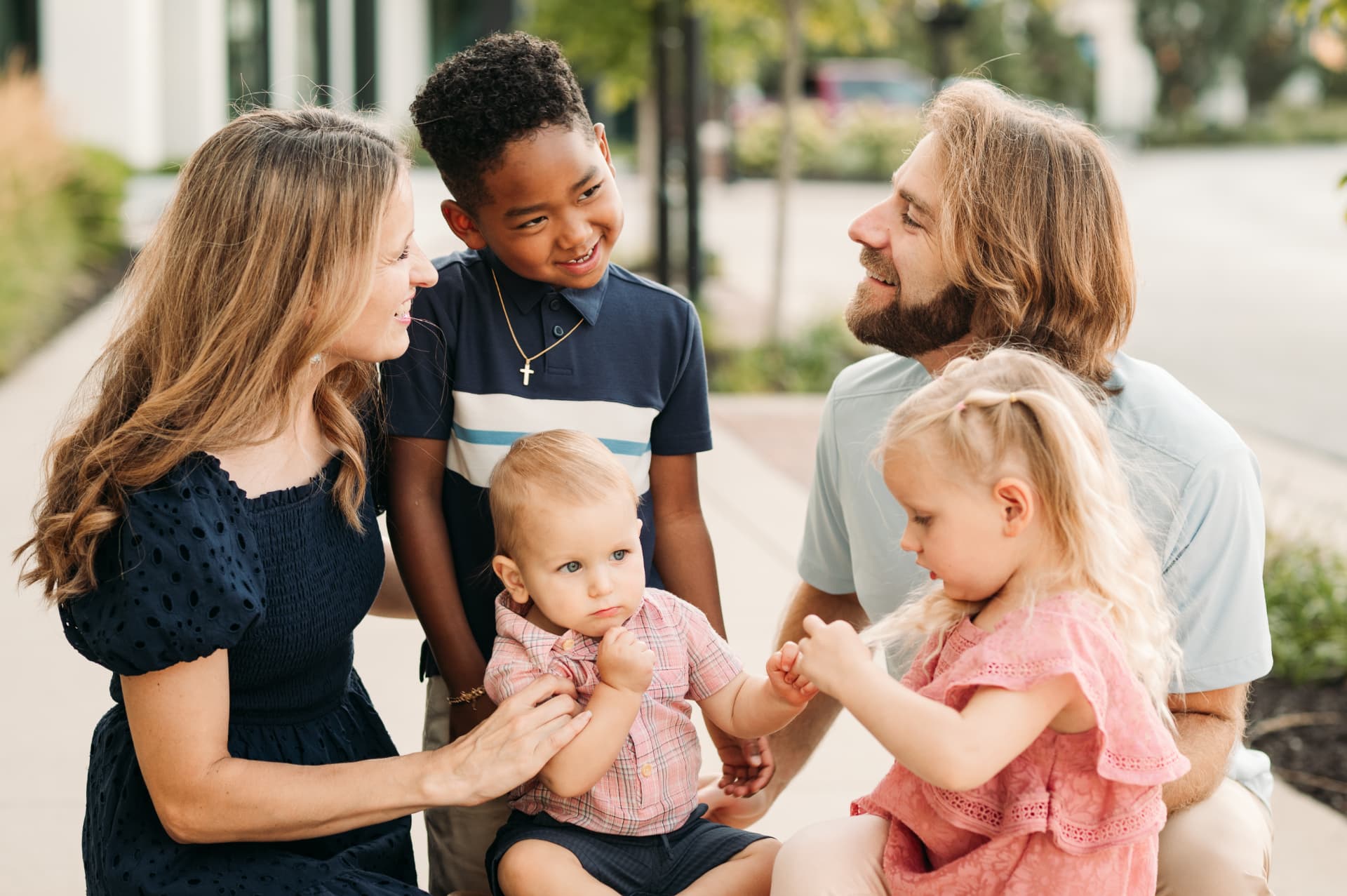 Family of five sitting together and laughing on a sidewalk at Lenexa City Center