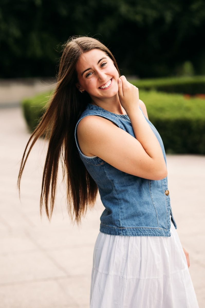 Senior girl in a denim vest smiling with her hair in the breeze by a garden path — seniors photography in the Kansas City area