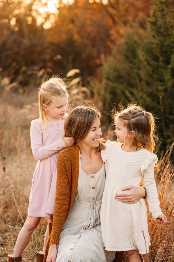 Mother laughing with her two daughters in a sunlit autumn field — family photography in the Kansas City area