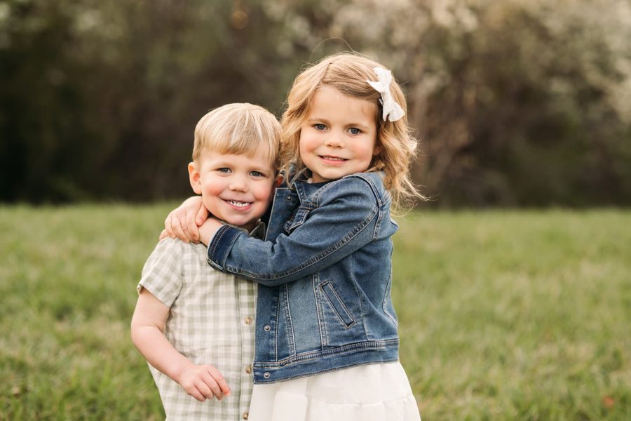 Big sister hugging her little brother in front of white spring blossoms — family photography in the Kansas City area