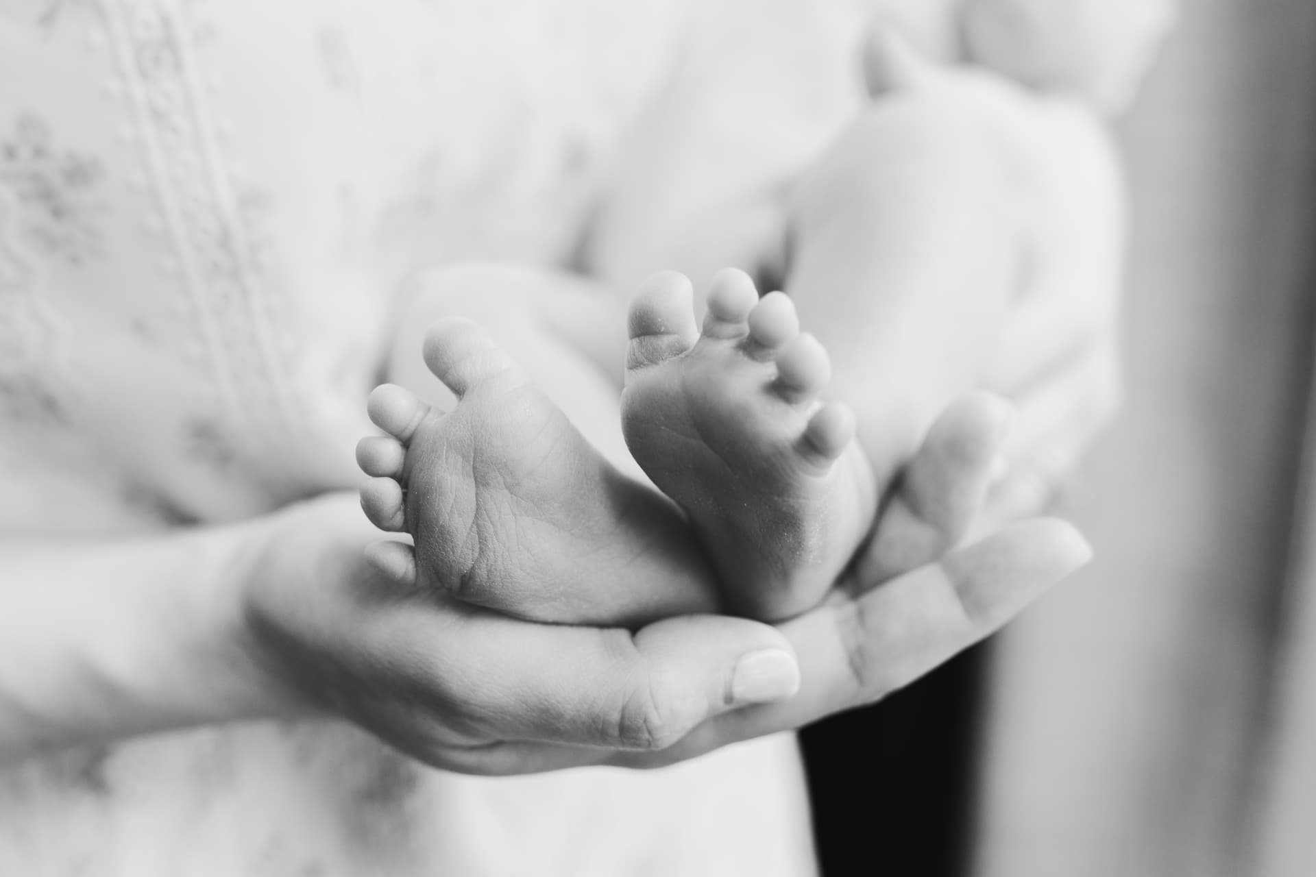 Black and white close-up of newborn feet cradled in a parent's hands