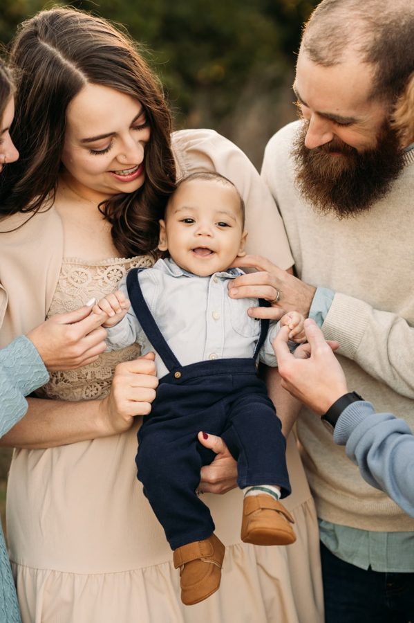 Parents helping their smiling baby boy stand in golden light — family photography in the Kansas City area