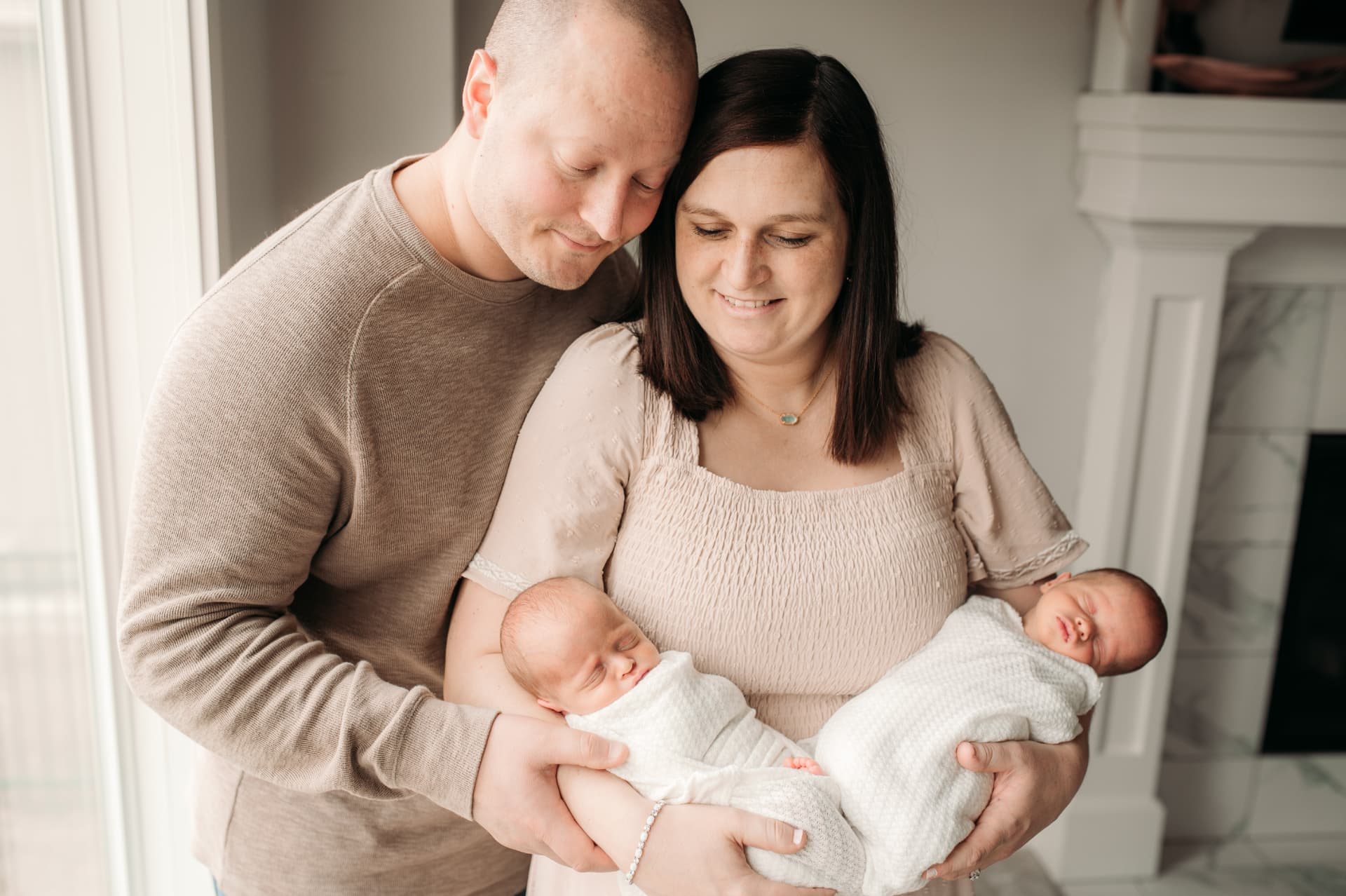 Parents holding their newborn twins in bright window light