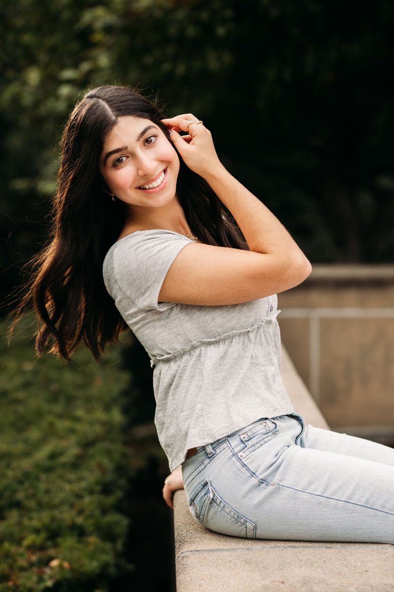 Senior girl smiling over her shoulder on a stone ledge in a park — seniors photography in the Kansas City area