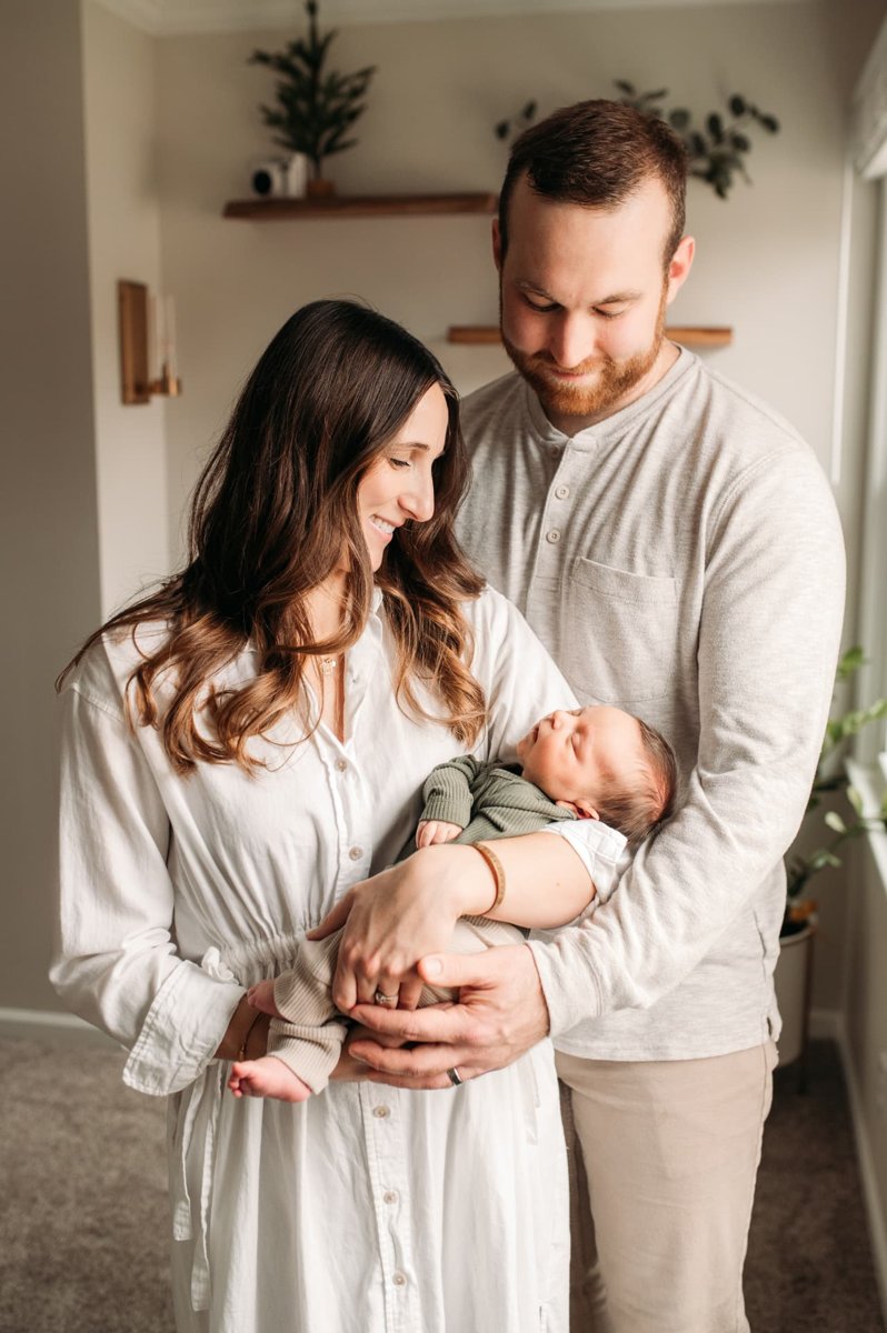 Parents holding their newborn son together in a sunlit nursery — newborn photography in the Kansas City area
