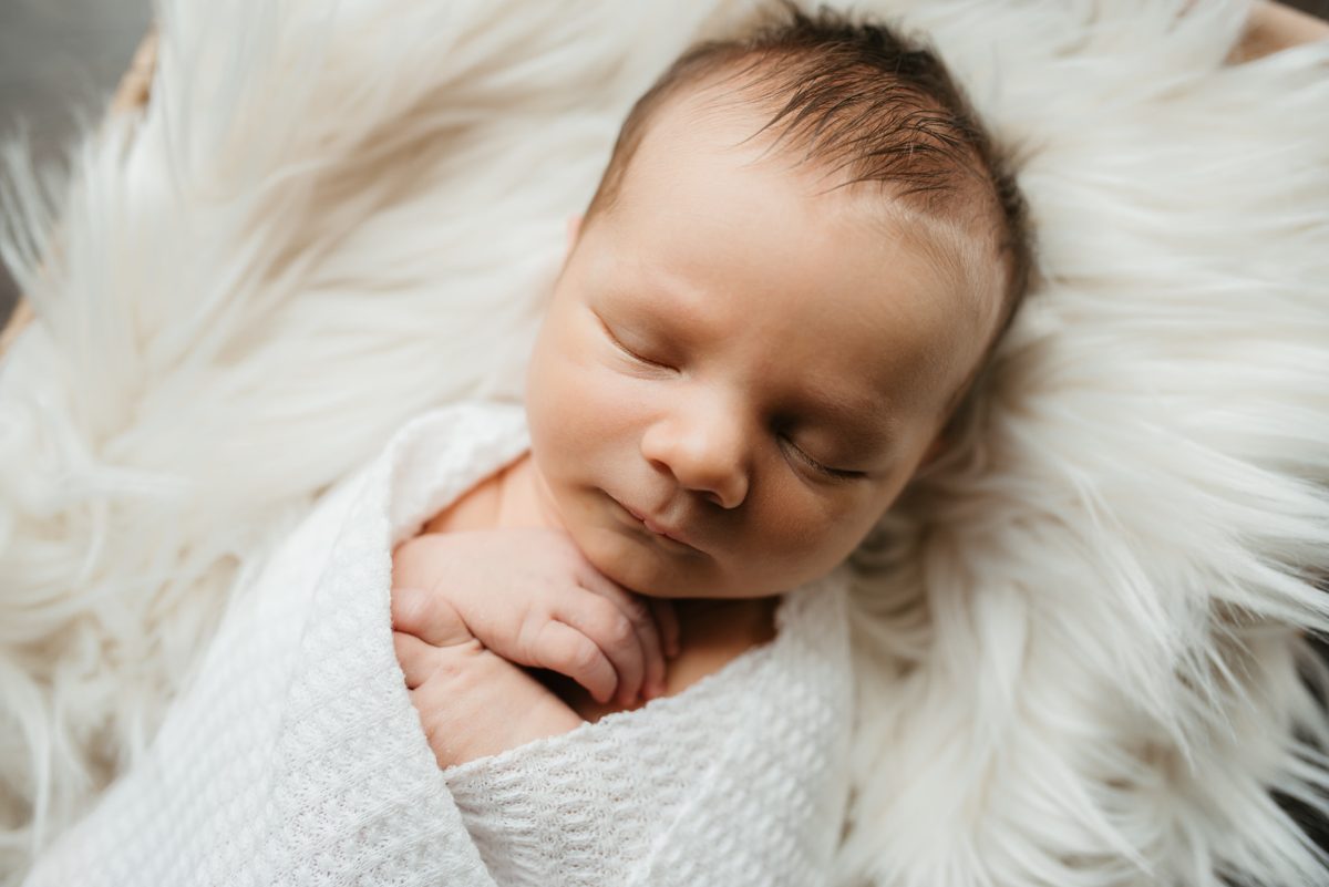Sleeping newborn swaddled in white with hands tucked under her chin — newborn photography in the Kansas City area