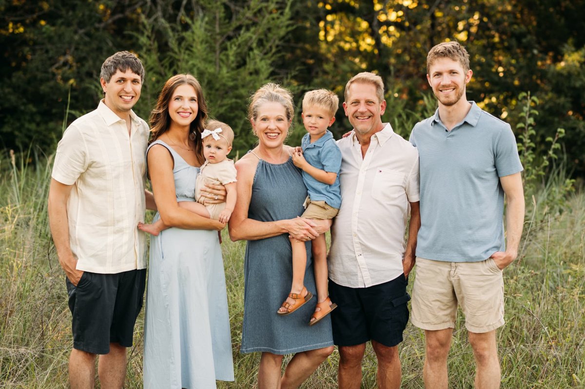 Grandparents holding their grandchildren beside their grown kids in a summer meadow