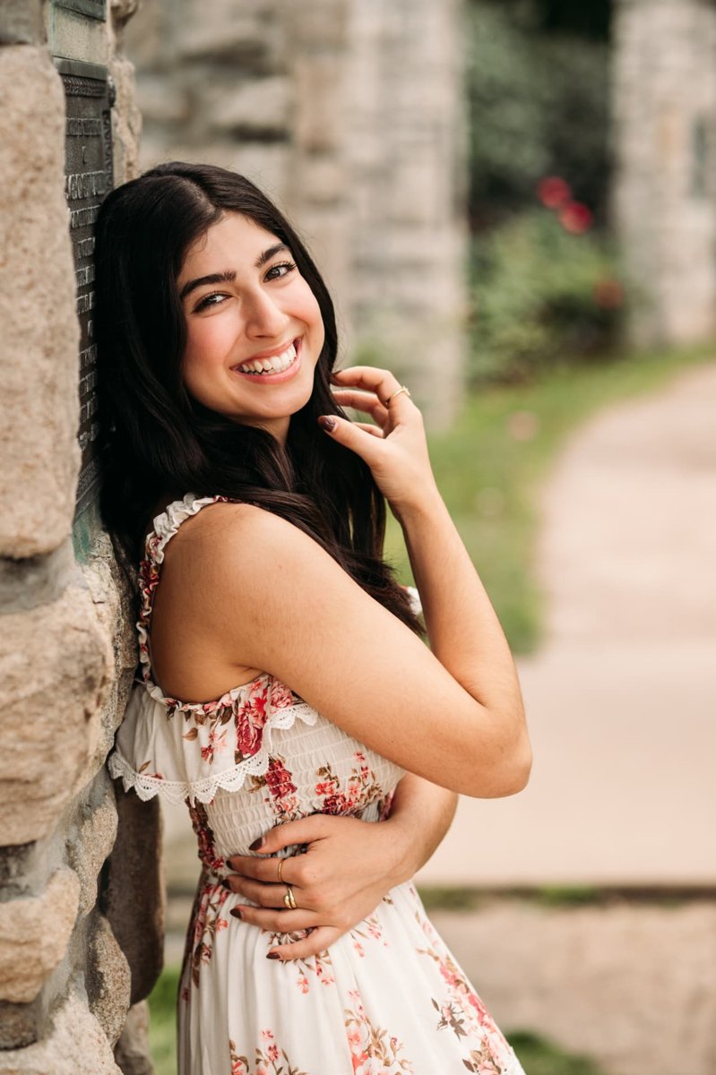 Senior girl in a floral dress laughing against a stone wall — seniors photography in the Kansas City area