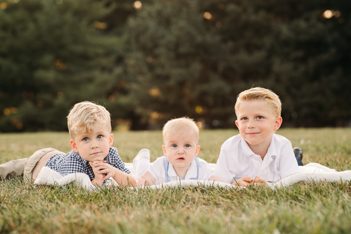 Three brothers lying on a blanket in the grass at sunset — family photography in the Kansas City area