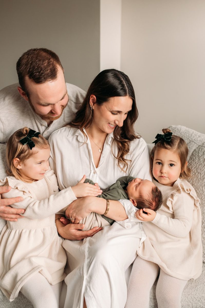 Parents and two big sisters admiring their newborn baby on the couch — newborn photography in the Kansas City area