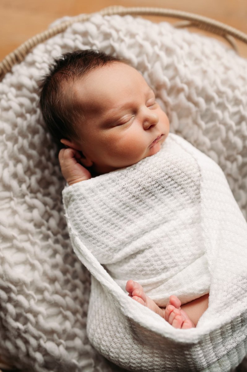 Sleeping newborn swaddled in white knit in a woven basket — newborn photography in the Kansas City area