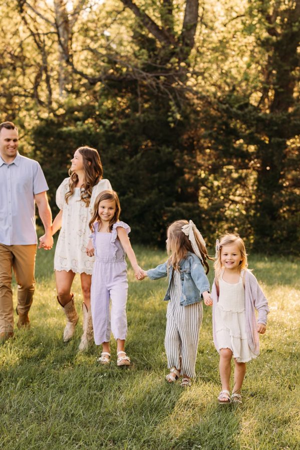 Family of five walking hand in hand through a green Kansas City meadow — family photography in the Kansas City area