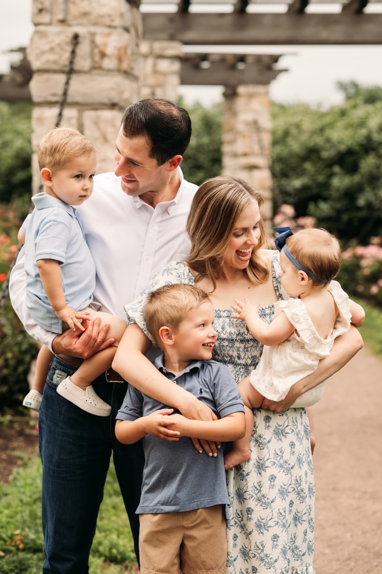 Family of five laughing together by the stone pergola at Loose Park Rose Garden in Kansas City