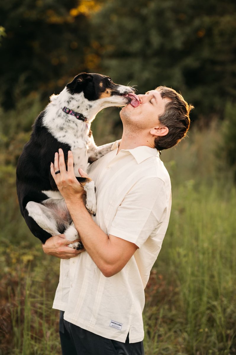 Dad lifting the family dog for a playful kiss in a summer field — family photography in the Kansas City area