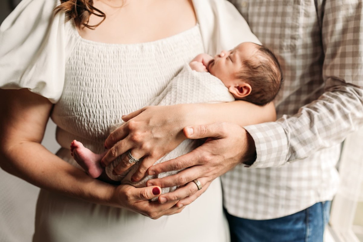Parents' hands cradling their sleeping newborn together — newborn photography in the Kansas City area