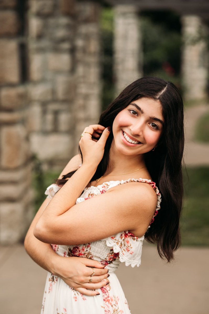 Senior girl in a floral dress smiling by stone columns — seniors photography in the Kansas City area